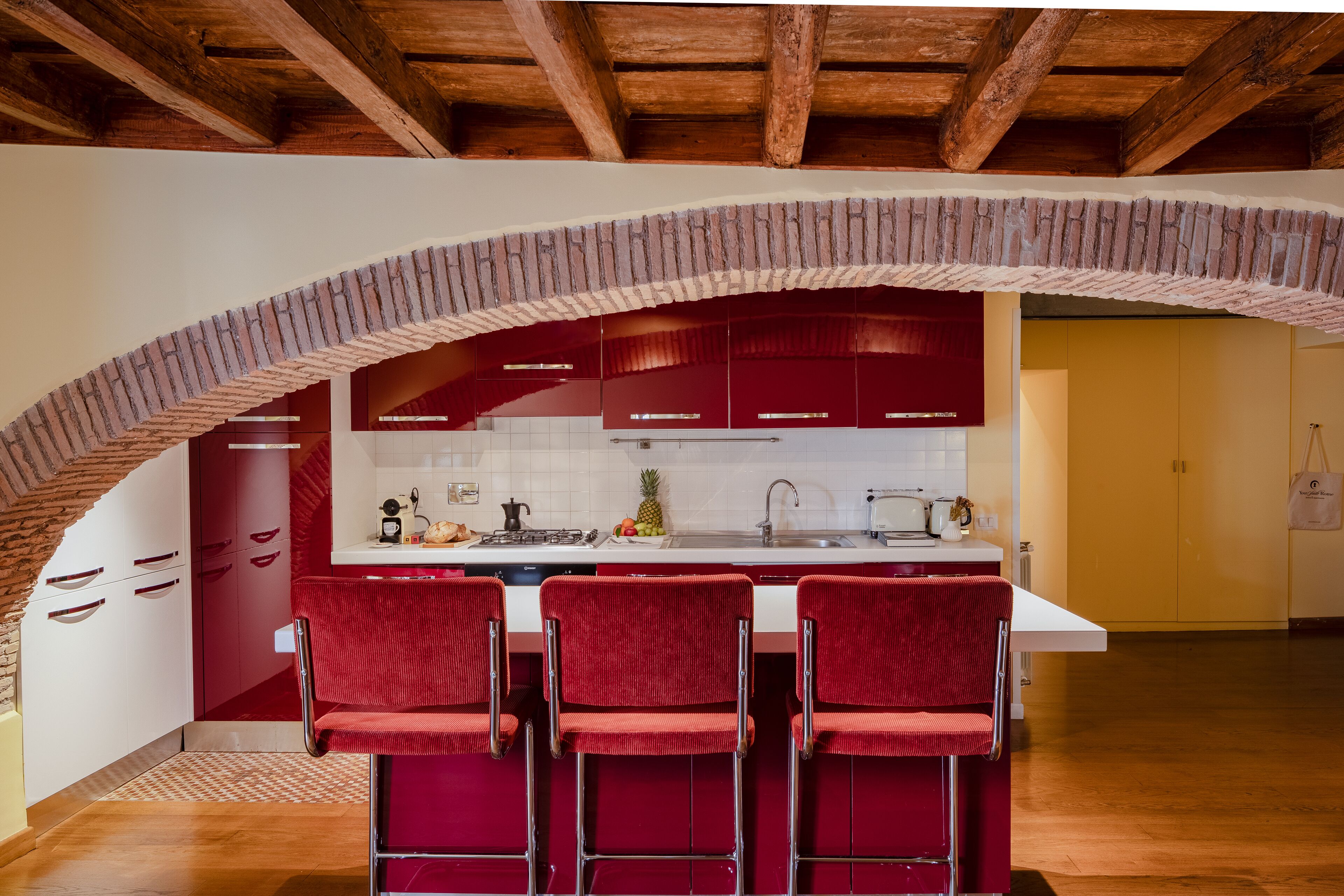 A kitchen with a brick arch, red cabinets, and a white countertop.