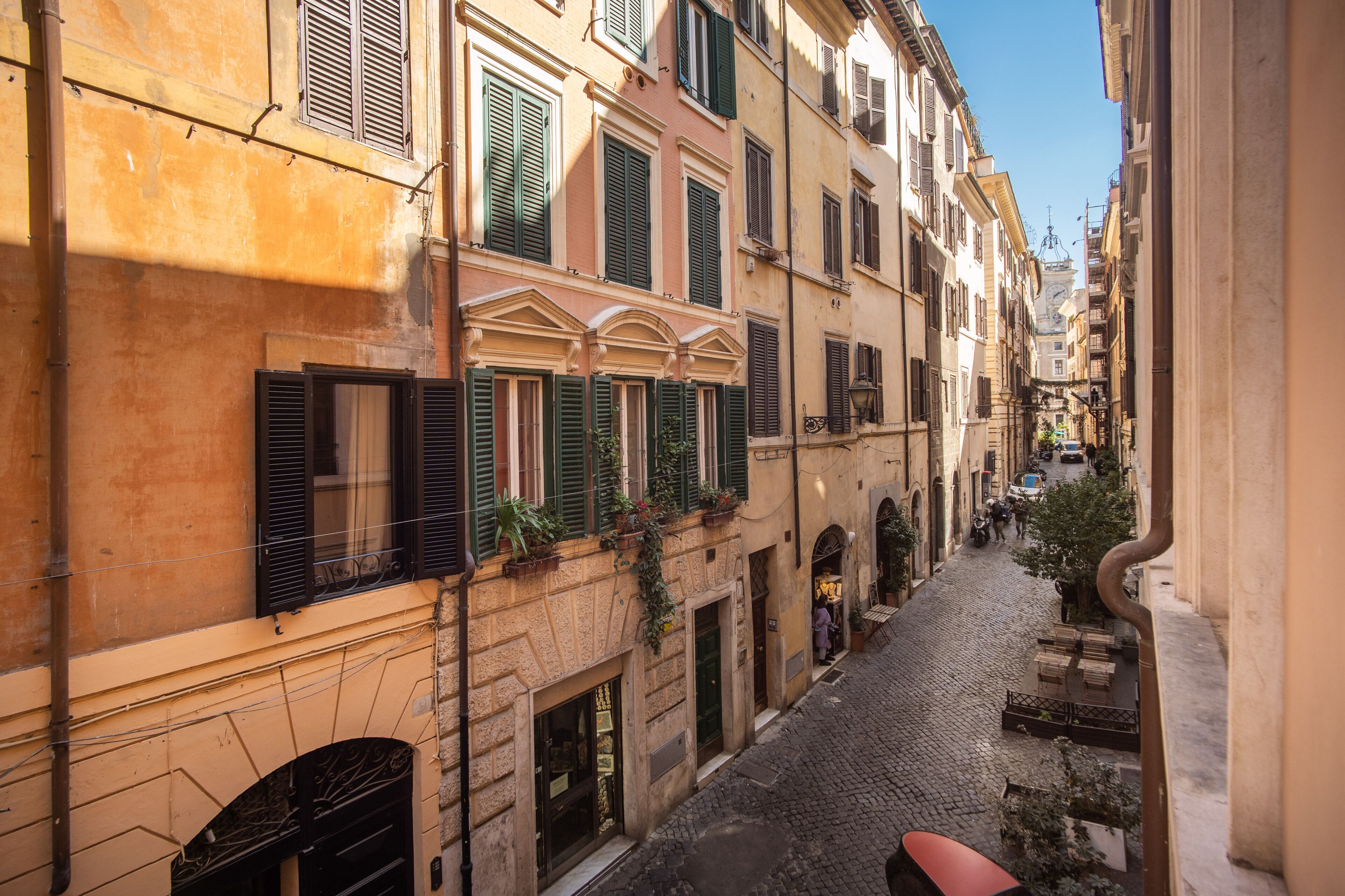 A narrow cobblestone street flanked by historic buildings with green shutters and arched doorways.
