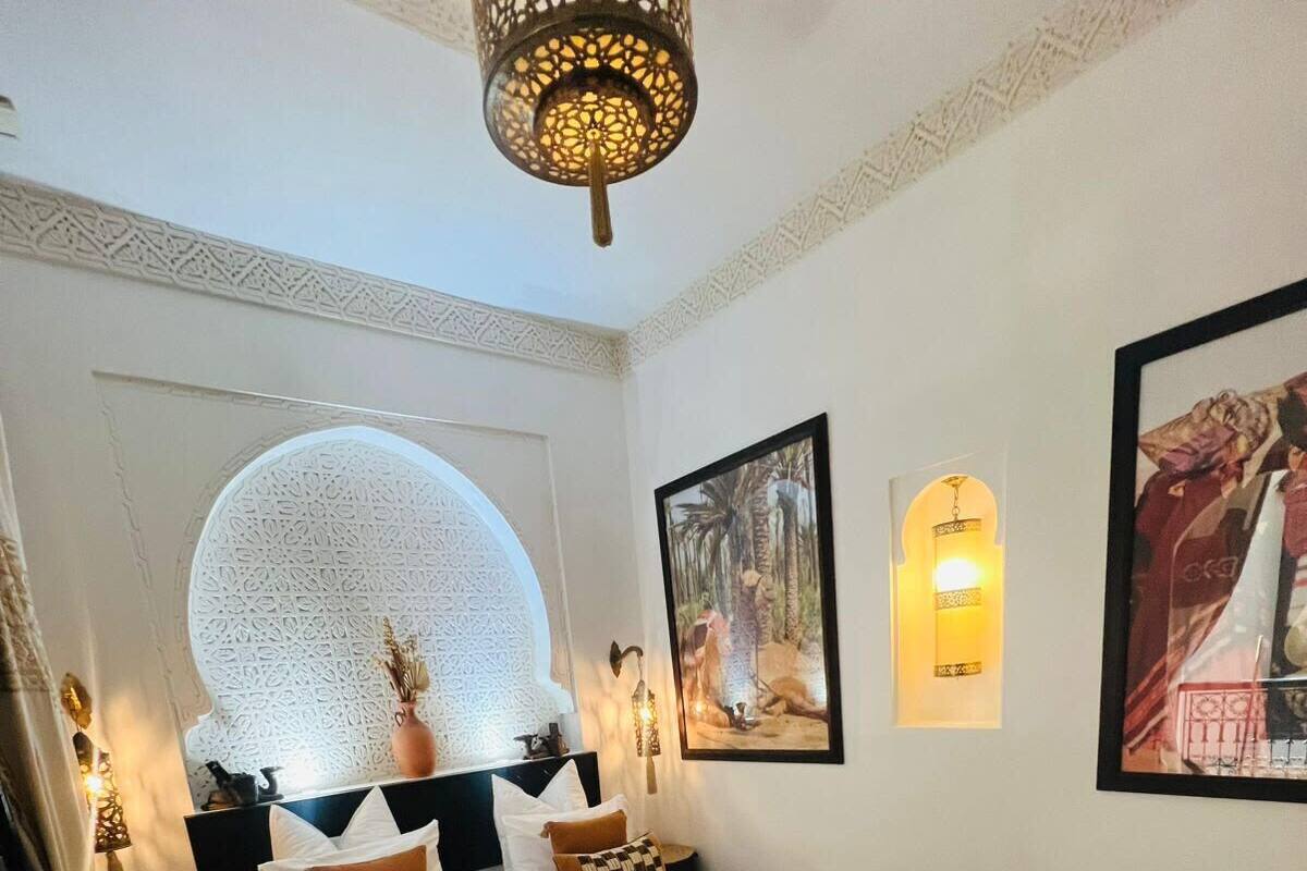 A bedroom with a large bed, a decorative ceiling light, wall-mounted lamps, and framed artwork.