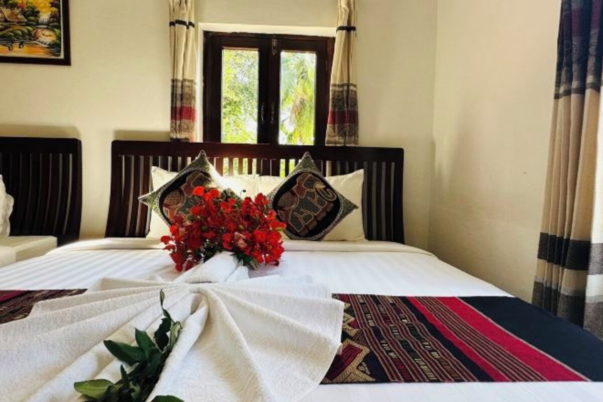 A neatly made bed with a floral arrangement, a patterned throw, and a window with curtains.
