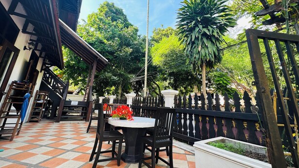 An outdoor patio with a checkered floor, a round table with chairs, and a decorative fence. - Thatsaphone Hotel (Luang Prabang)