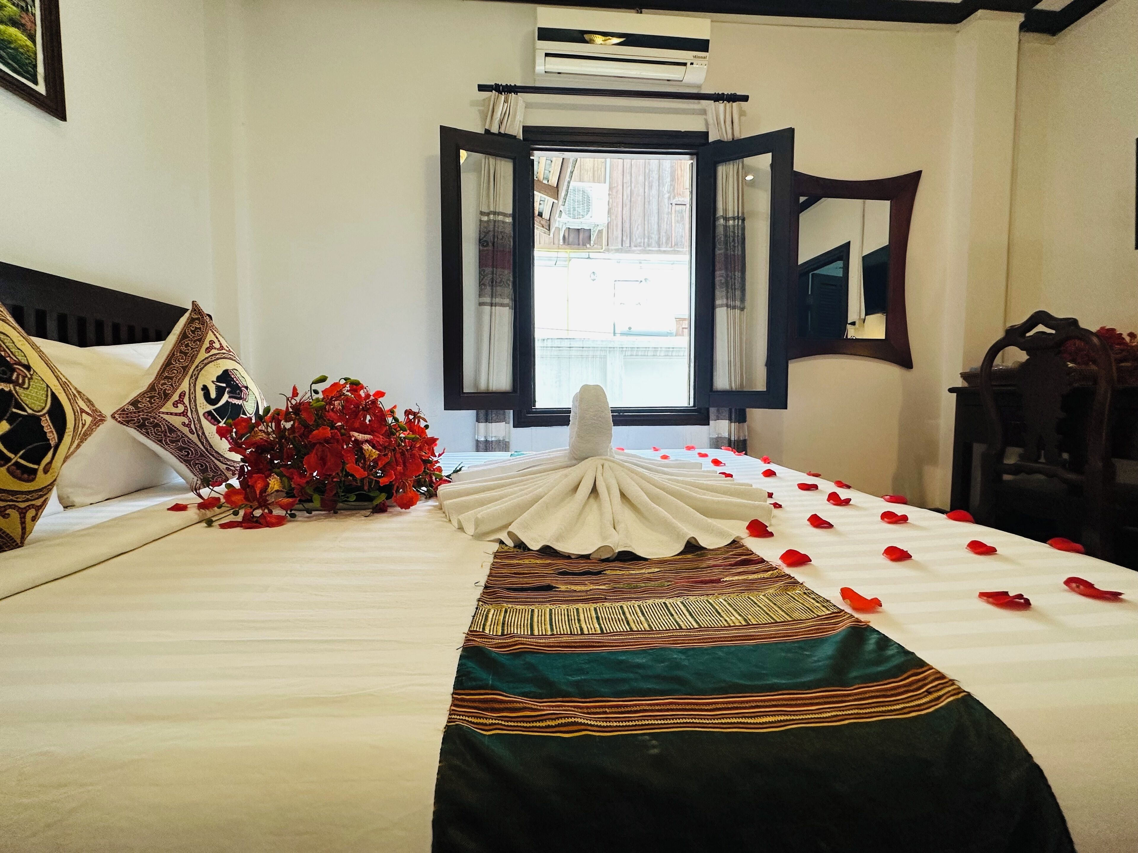 A neatly made bed with a decorative pillow, a vase of red flowers, and a bedspread with a geometric pattern.