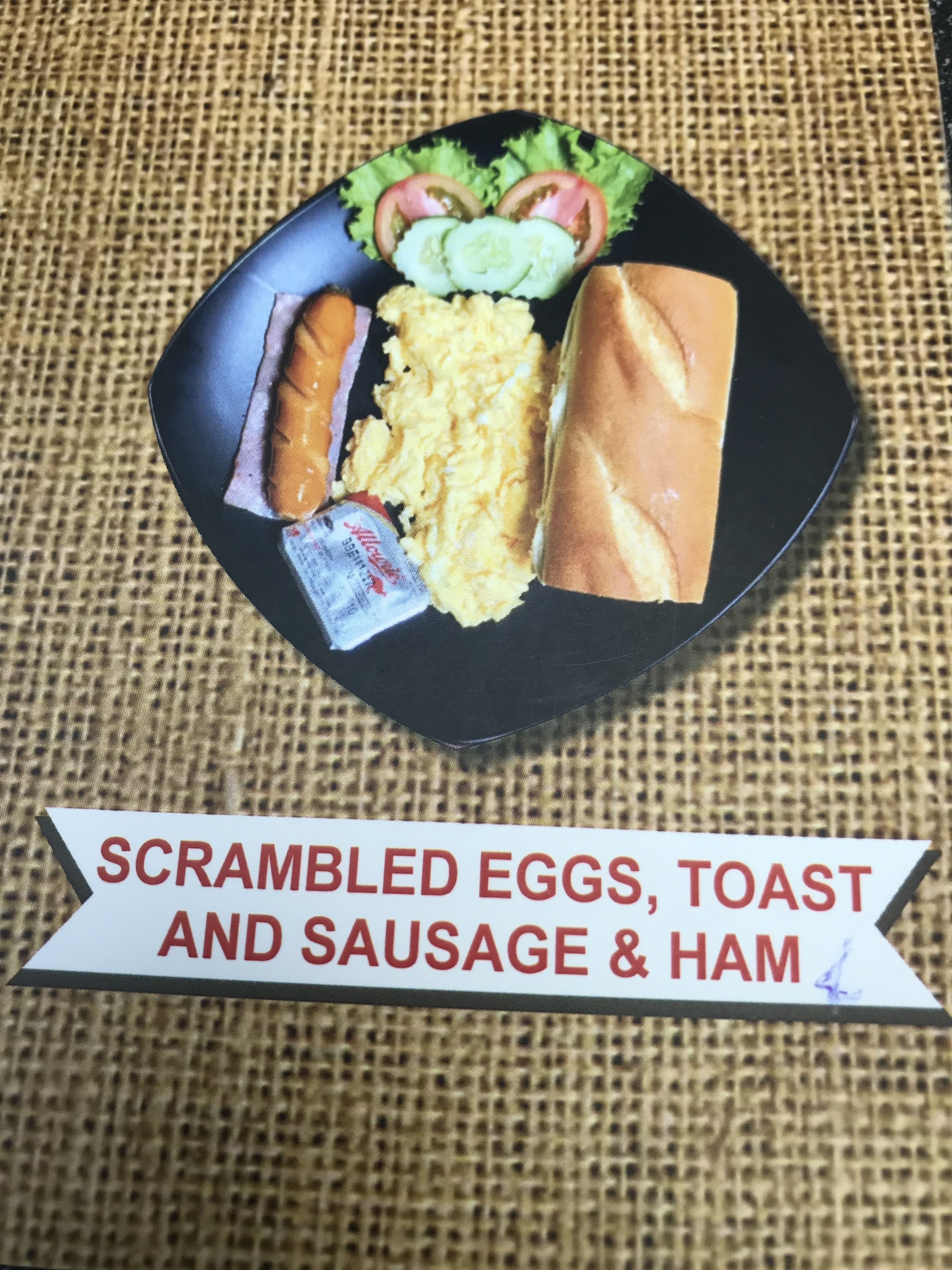 A meal consisting of scrambled eggs, toast, sausage, and ham on a black plate.