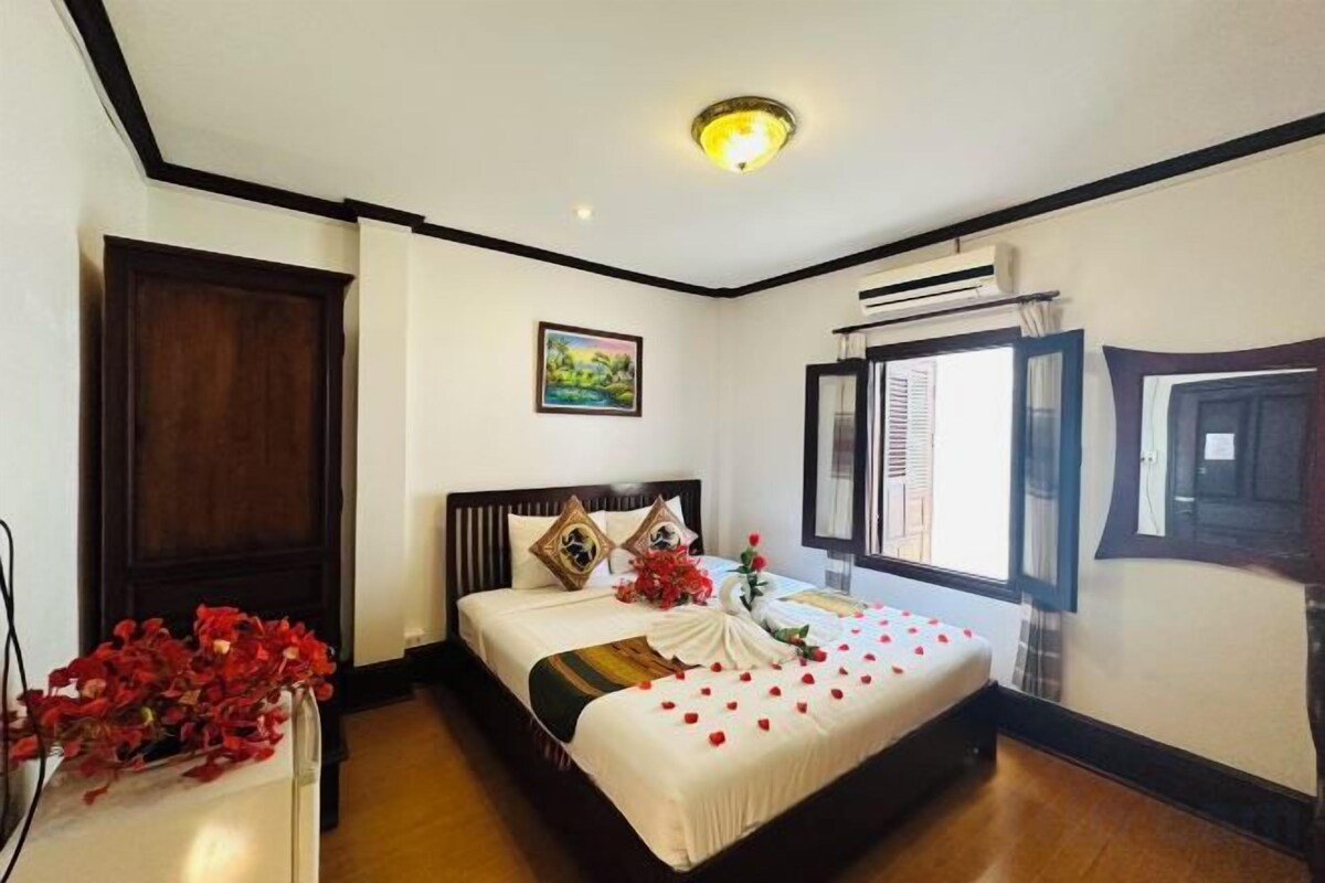 A bedroom with a bed, a nightstand, a window with blinds, and a wall-mounted air conditioning unit.