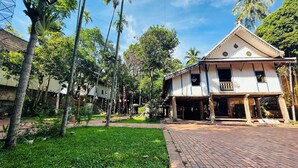 A traditional building with a tiled roof, surrounded by lush greenery and palm trees. - Thatsaphone Hotel (Luang Prabang)