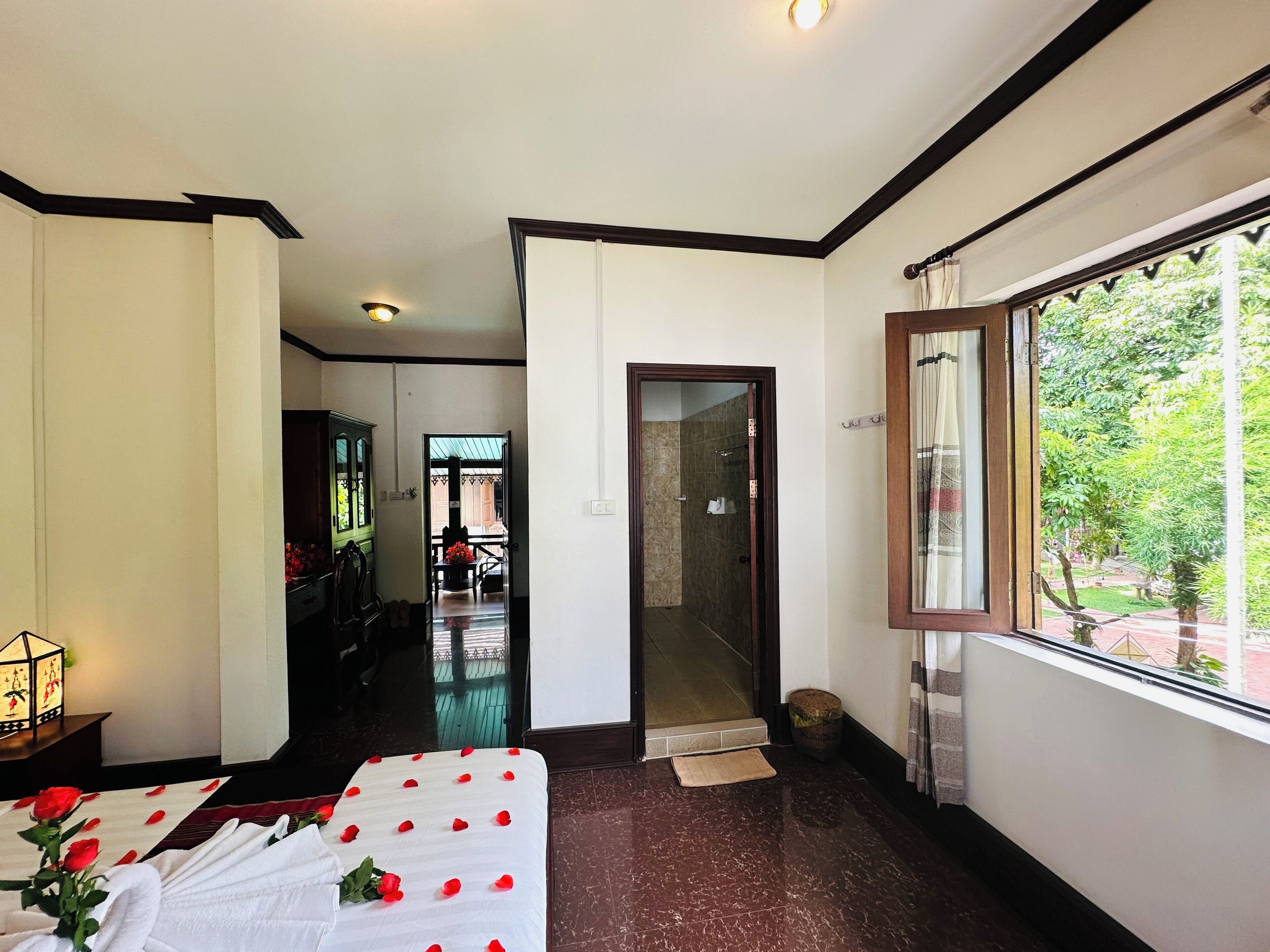 Habitación de hotel con cama, ventana con vistas a zonas verdes, baño con ducha y pasillo que conduce a otra habitación.