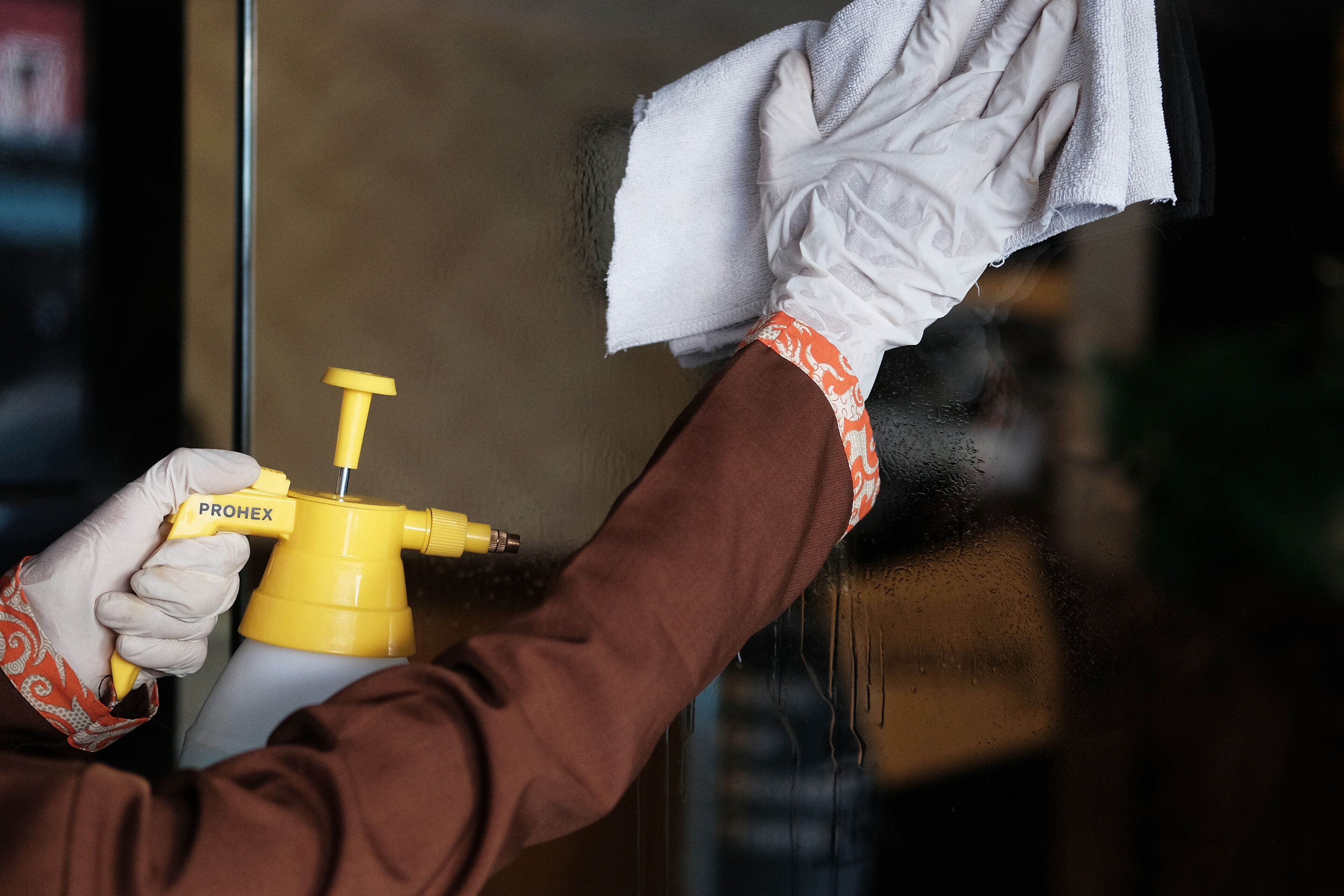 Eine Person reinigt ein Fenster mit einer gelben Sprühflasche und einem Tuch.