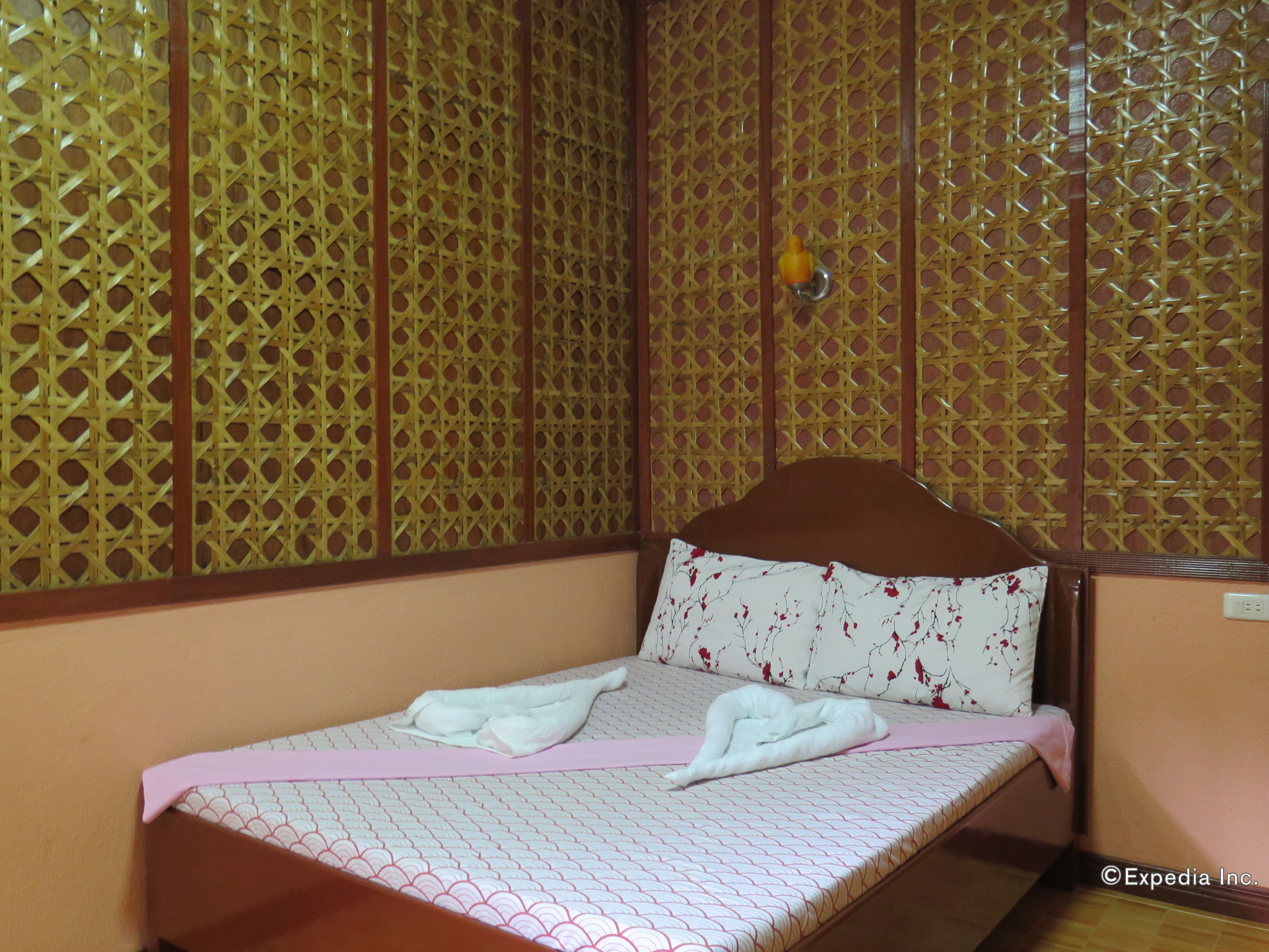 Una habitación con una cama, un panel divisor de madera y una lámpara fijada a la pared.