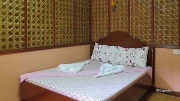 Una habitación con una cama, un panel divisor de madera y una lámpara fijada a la pared.