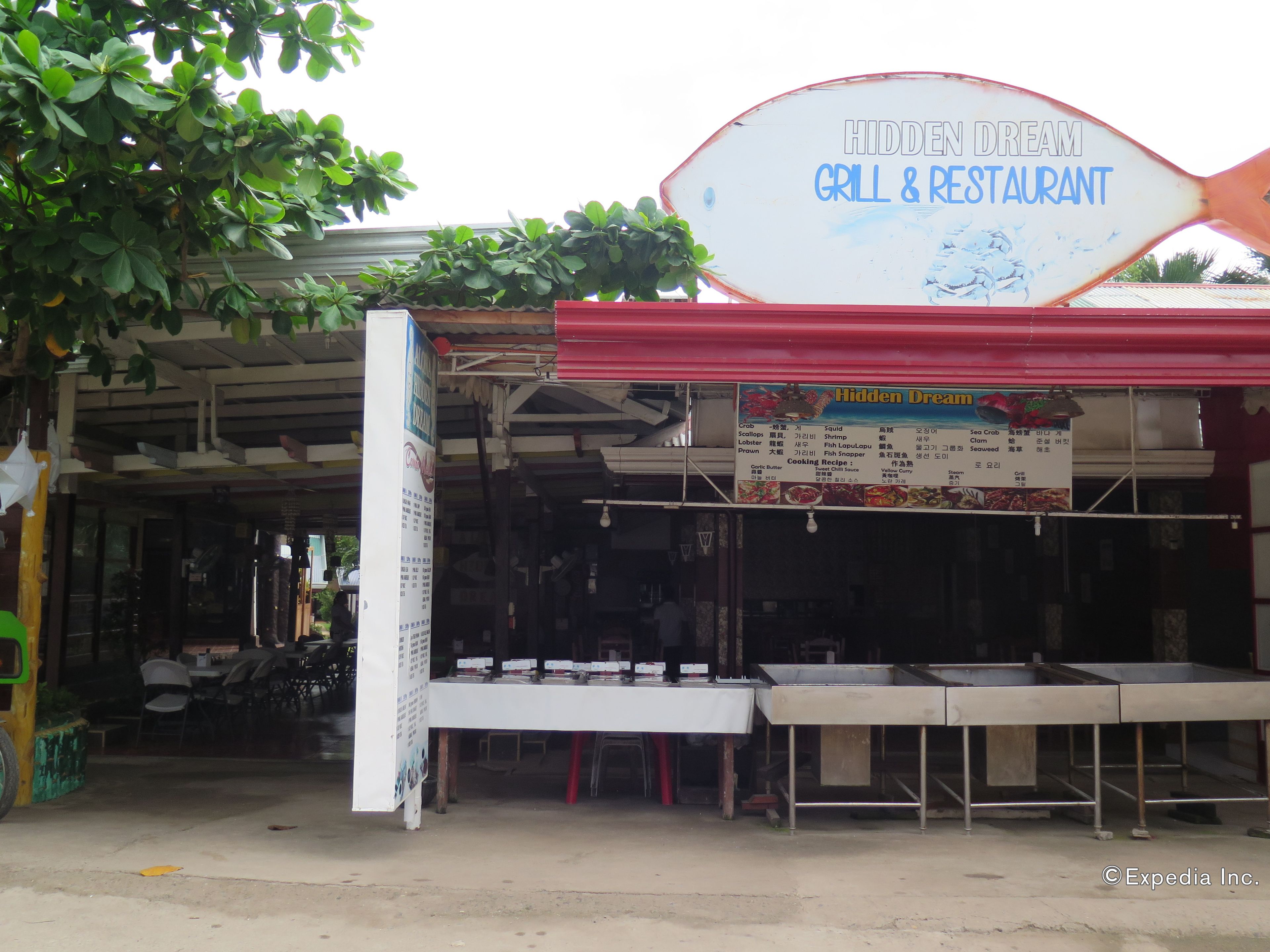A restaurant with a sign reading "Hidden Dream Grill & Restaurant" and a menu board listing seafood dishes.