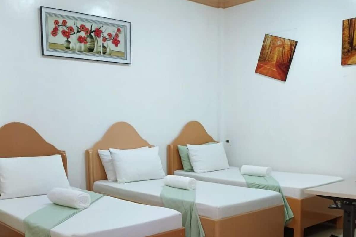A hotel room with three single beds, a small table, and a desk.