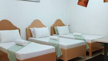 A hotel room with three single beds, a small table, and a desk.