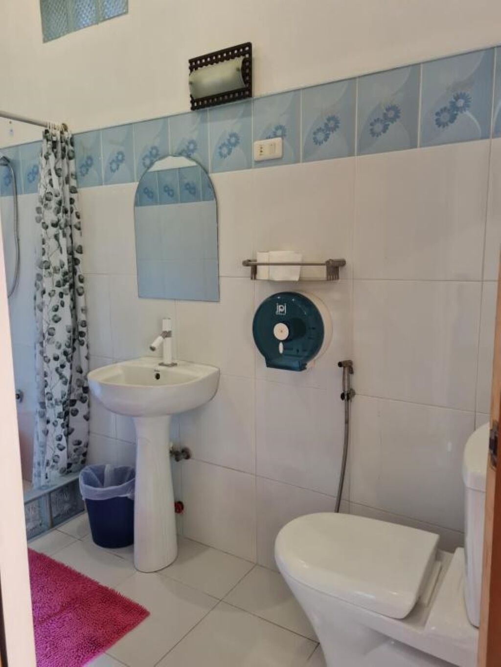 Baño con lavamanos blanco, inodoro, ducha y cortina de ducha azul estampada.