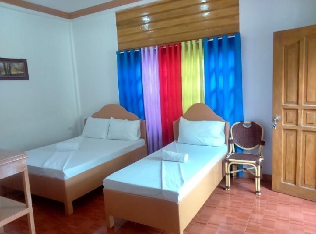 A room with two single beds, a wooden chair, and a wooden door.