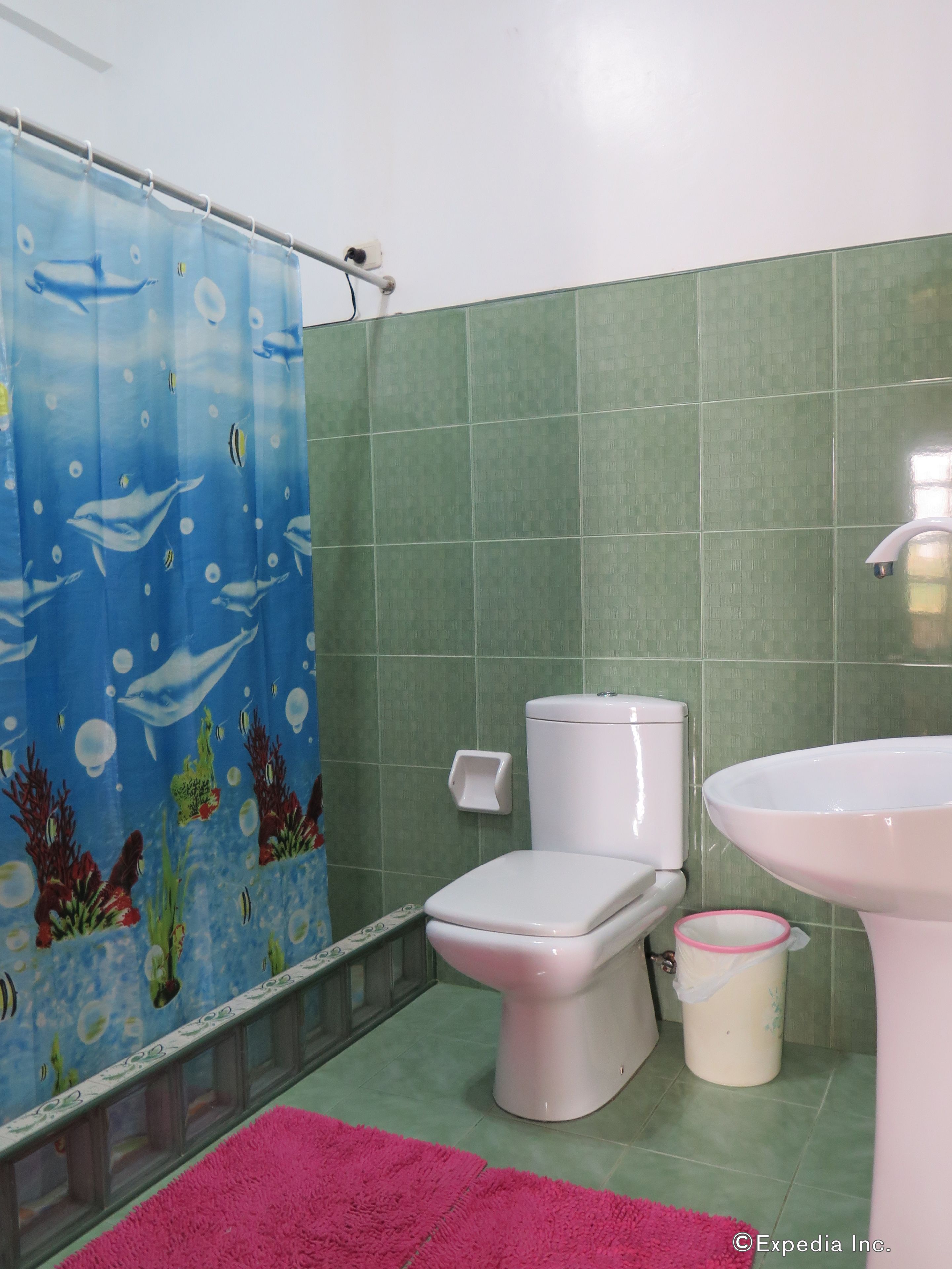 A bathroom with a shower curtain featuring an underwater scene, a toilet, a sink, and a trash can.