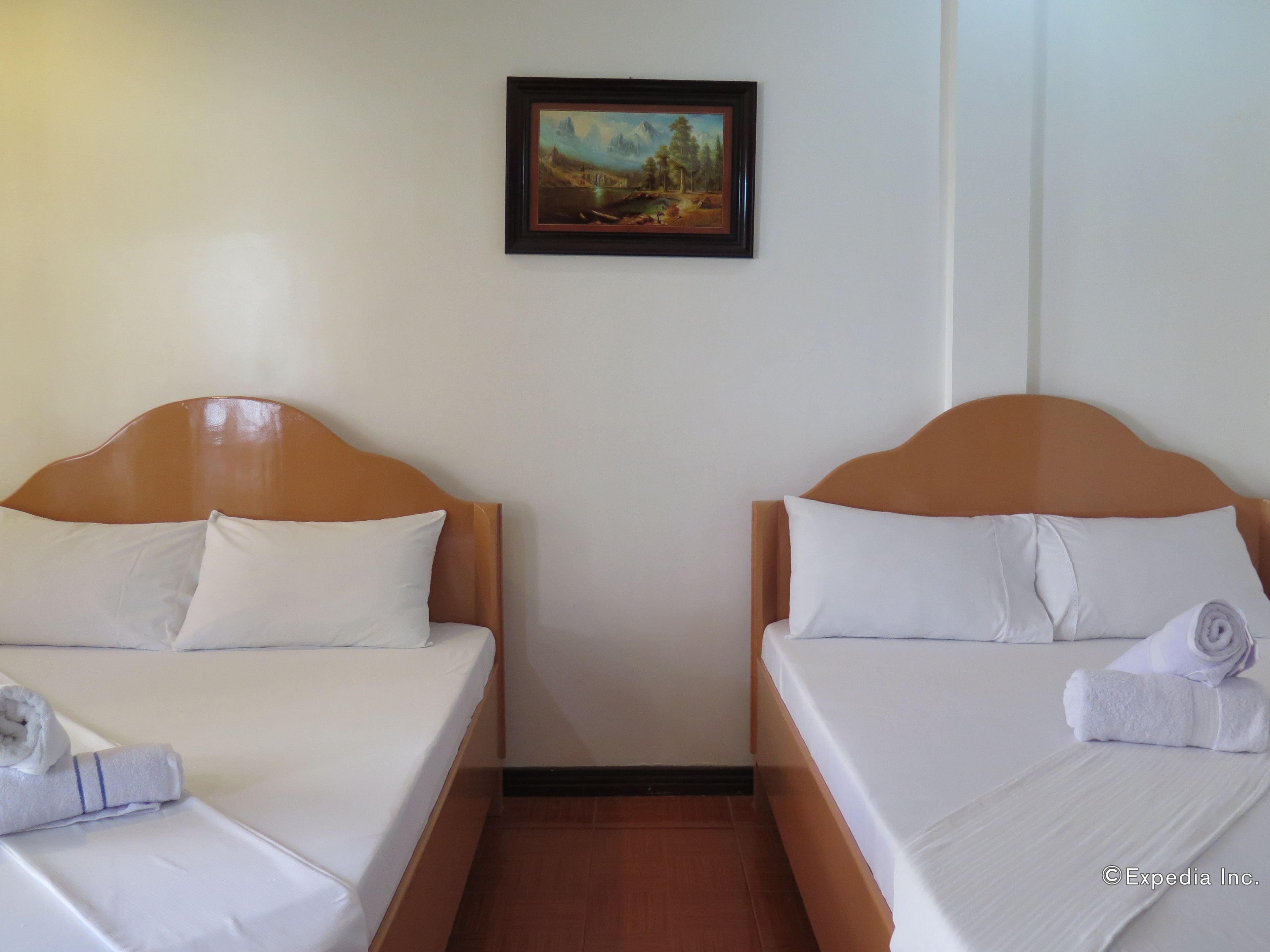 A hotel room with two single beds, white linens, and a painting on the wall.
