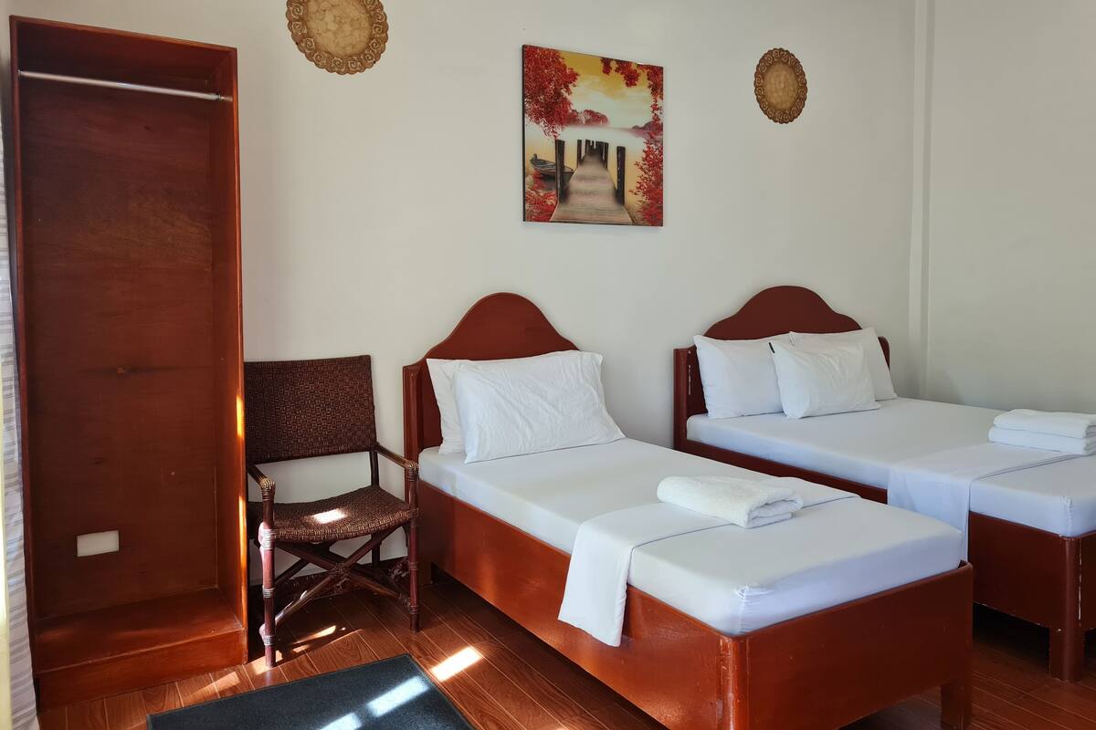 A hotel room with two single beds, a wooden chair, a door, and two wall decorations.