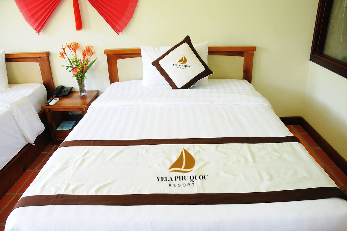 A hotel room with a bed, a nightstand with a phone and remote, and a vase with flowers.