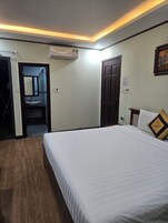 Una habitación de hotel con cama, puerta, equipo de aire acondicionado y una mesita de noche.