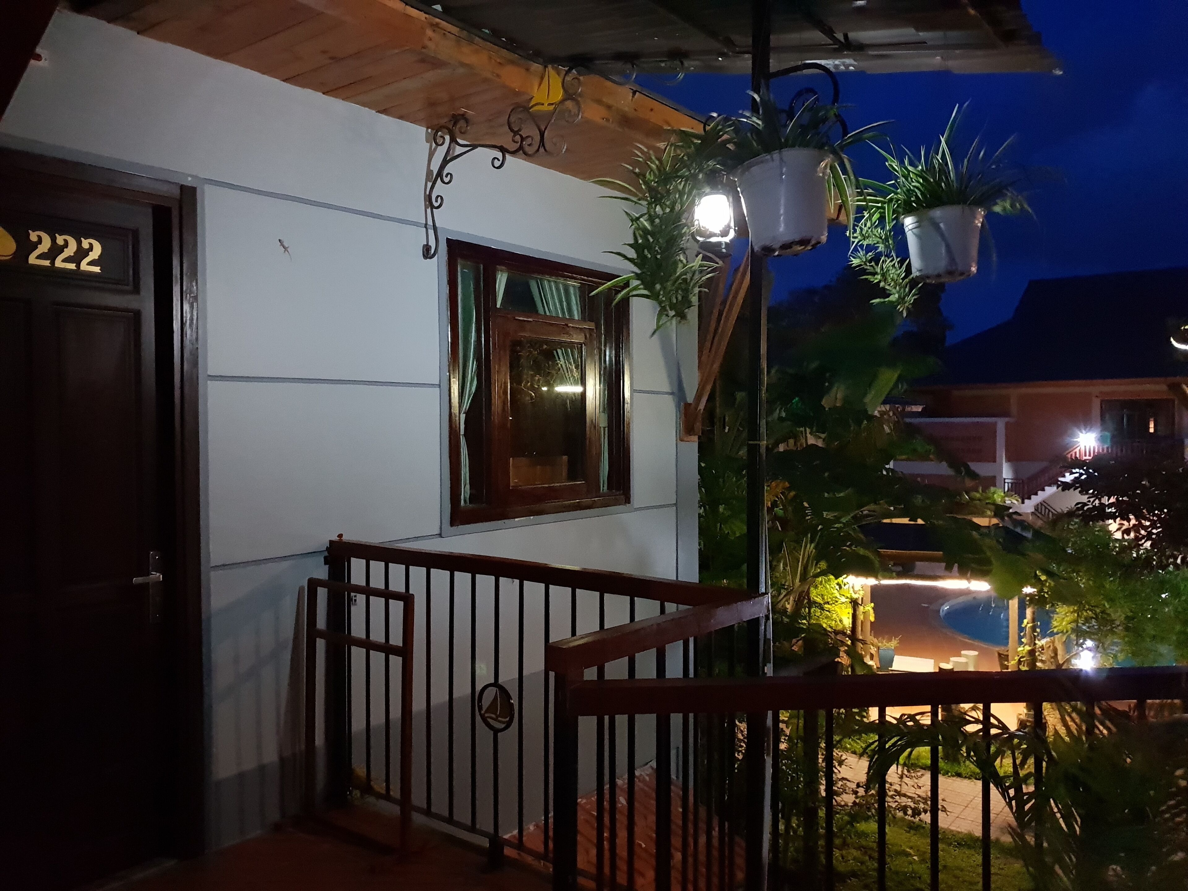 Uma casa com o número '222' na porta, uma varanda com grade e plantas em vasos.