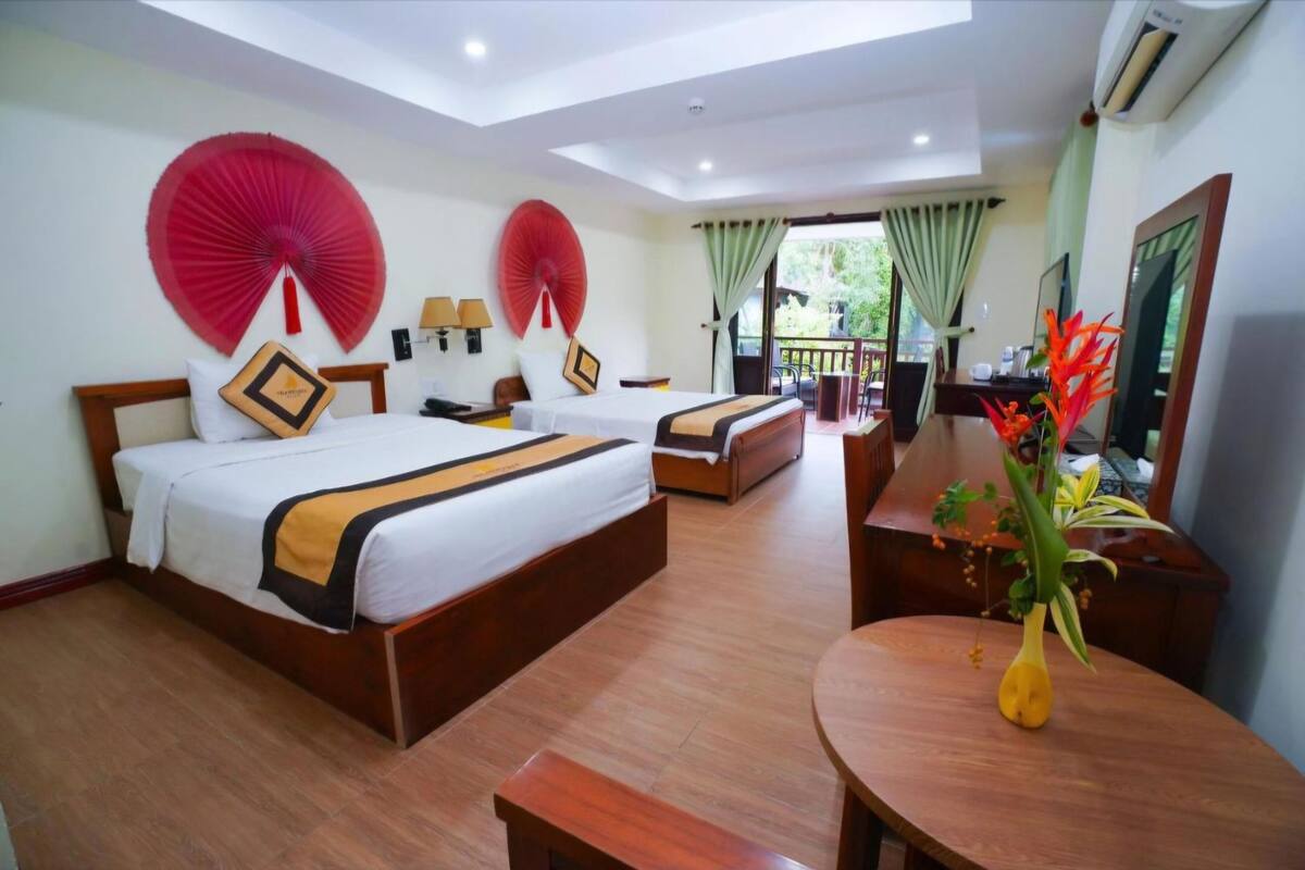 A hotel room with a large bed, a desk, a chair, and a small table with a vase of flowers.