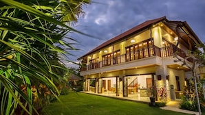 Une maison à deux étages avec un balcon, une pelouse bien entretenue et un pilier en pierre.