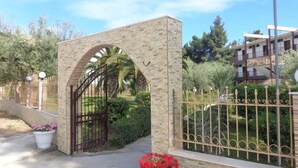A gated entrance with a stone archway, a metal gate, and a potted plant with red flowers. - Porto Matina Hotel (Polygyros)