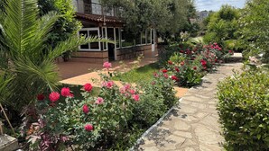 A garden pathway lined with pink flowers and green shrubs, leading to a building with a tiled roof and a balcony. - Porto Matina Hotel (Polygyros)