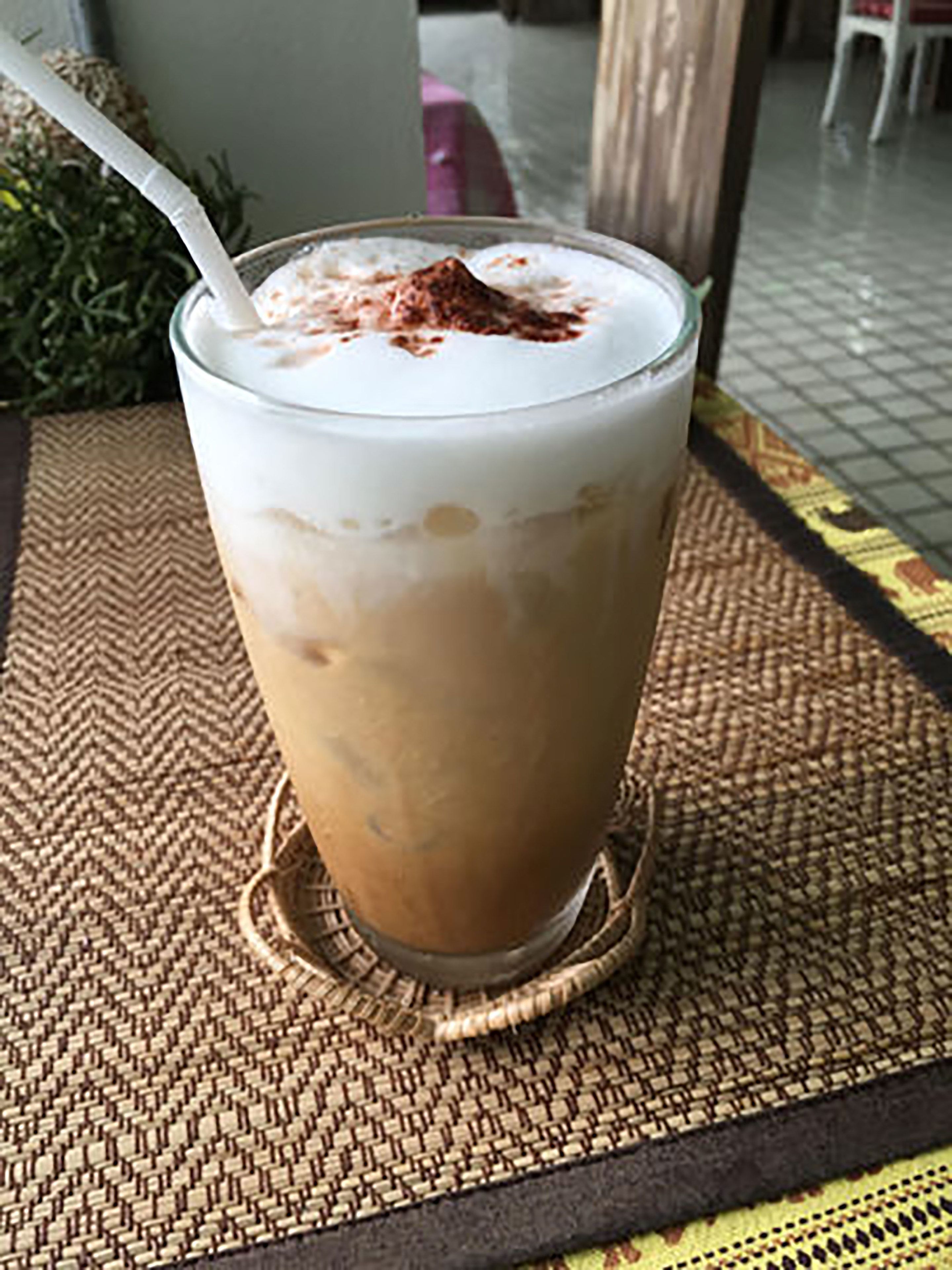 Un got de cafè helat amb nata i un pols de cacao sobre un suport trenat.