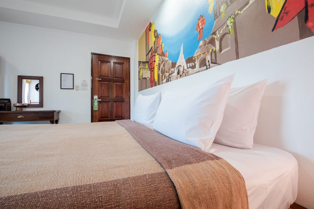 Ein Hotelzimmer mit einem großen Bett, einer Holztür, einem Spiegel und einem Wandbild.