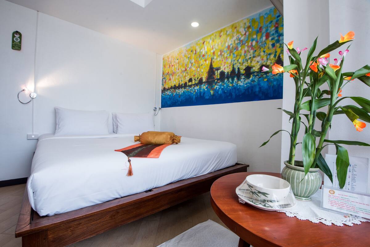 Ein Hotelzimmer mit Bett, einem Bild an der Wand, einem Tisch mit Blumenvase und einem Schild.
