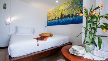 A hotel room with a bed, a painting on the wall, a table with a vase of flowers, and a sign.
