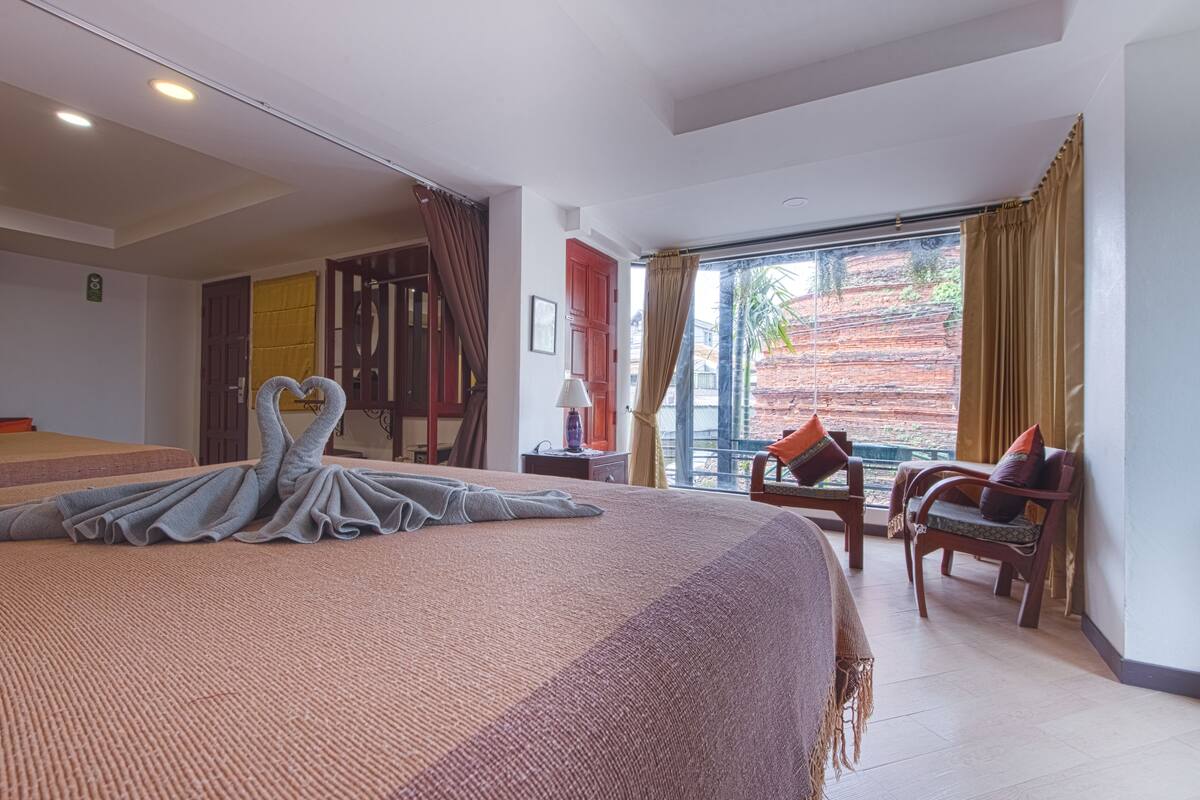 Ein Hotelzimmer mit einem großen Bett, einer Sitzecke mit Sesseln, einem Fenster mit Vorhängen und Blick nach draußen.