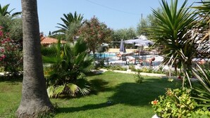 Área de piscina com espreguiçadeiras e guarda-sóis, rodeada por palmeiras e plantas floridas.