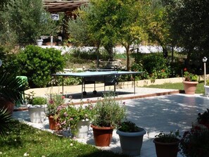 Un jardín con mesa de ping pong, plantas en macetas y una pérgola.