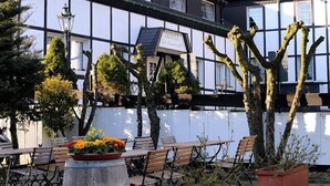 An outdoor seating area with wooden tables and chairs, surrounded by potted plants and trees. - Hotel Gut Moschenhof (Düsseldorf)