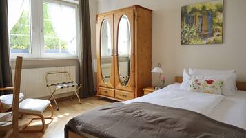 Un dormitorio con una cama, un armario de madera, una silla, un radiador y una ventana con cortinas.