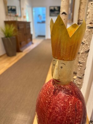 A wooden sculpture with a crown and a red textured body, placed on a wooden floor in a room with a wooden cabinet and a plant in the background. - Hotel Gut Moschenhof (Düsseldorf)