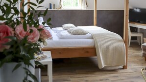 A bedroom with a wooden four-poster bed, a bedside table, a TV, and a potted plant. - Hotel Gut Moschenhof (Düsseldorf)
