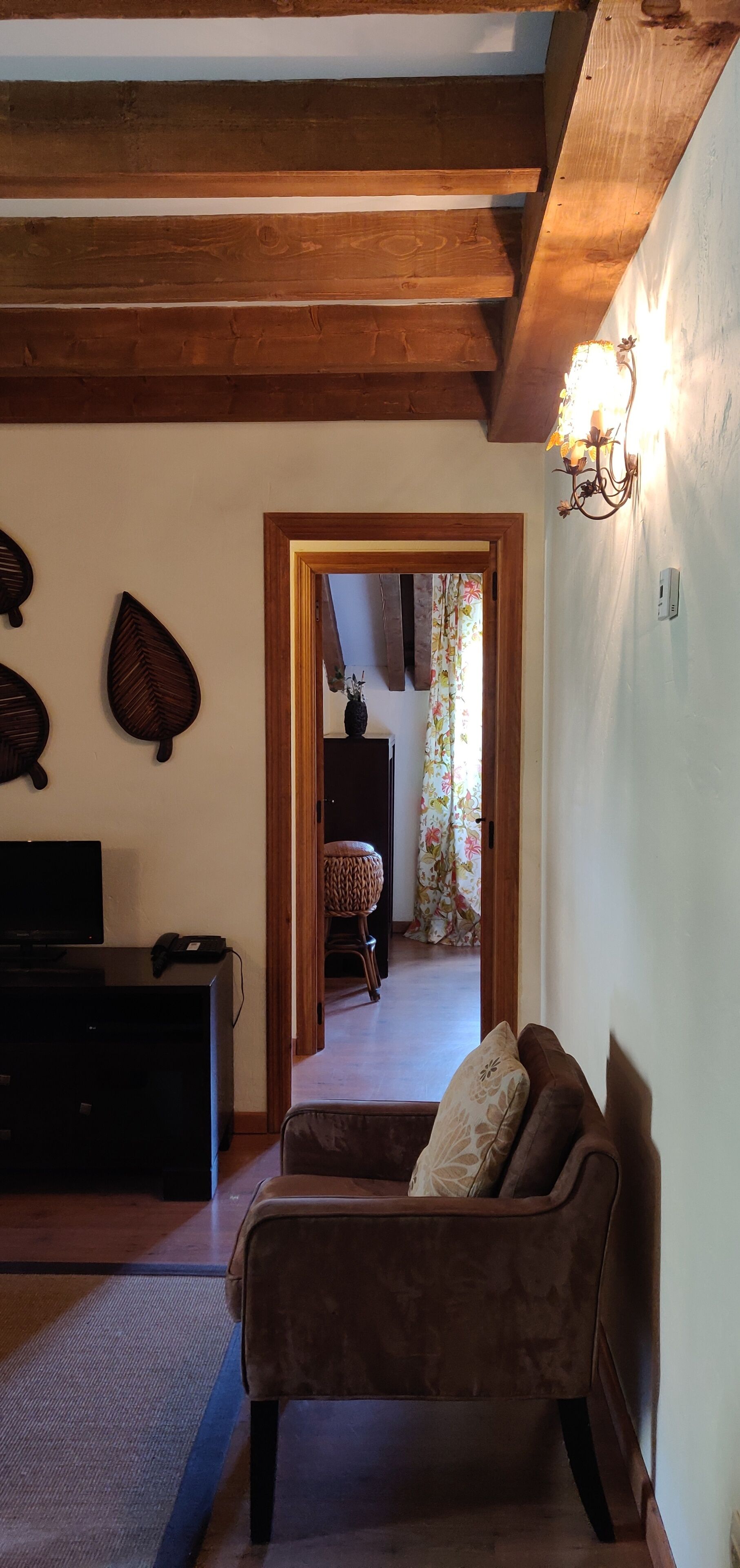 A living room with a brown sofa, a television, and wooden beams on the ceiling.