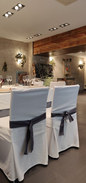 A dining area with white tablecloths, chairs with dark sashes, and recessed ceiling lights.