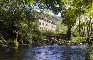 A building with a traditional architectural style, surrounded by lush greenery and a flowing river.