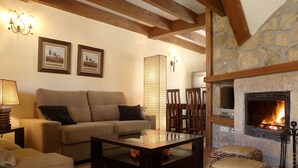 A cozy living room with a stone fireplace, wooden beams, a sofa, a coffee table, and a TV. - Hotel Ribera del Corneja (Navacepedilla de Corneja)