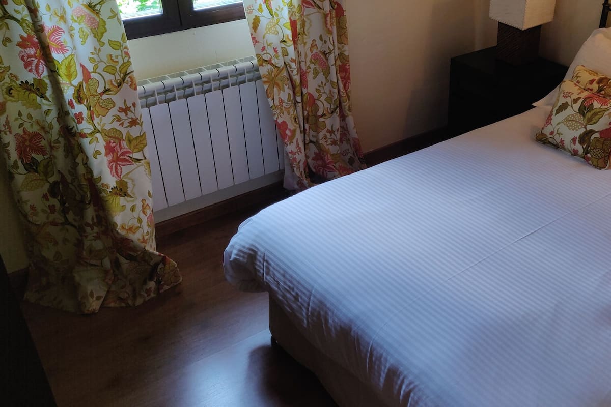 A neatly made bed with floral-patterned pillows, a white headboard, and a window with curtains.