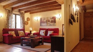A living room with a red sofa set, a coffee table, and a lamp. There are wooden beams on the ceiling and a door with a coat rack. - Hotel Ribera del Corneja (Navacepedilla de Corneja)