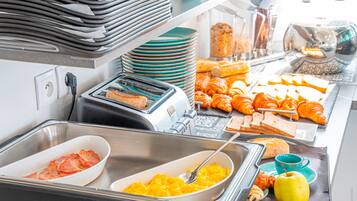 Un buffet proposant une variété d’aliments, notamment du pain, des croissants et des fruits.
