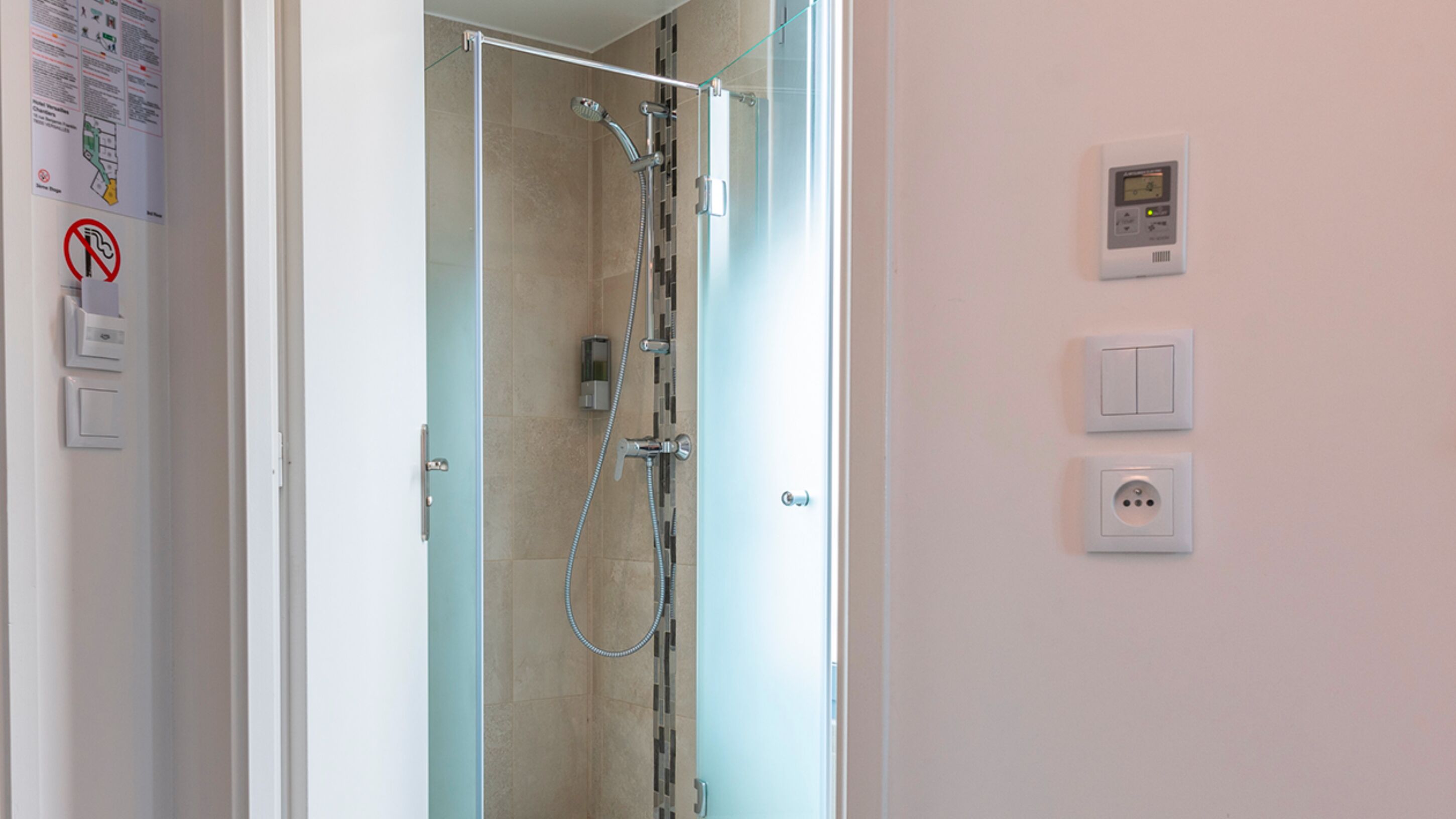 A modern bathroom with a glass shower enclosure, a wall-mounted control panel, and a door with a handle.