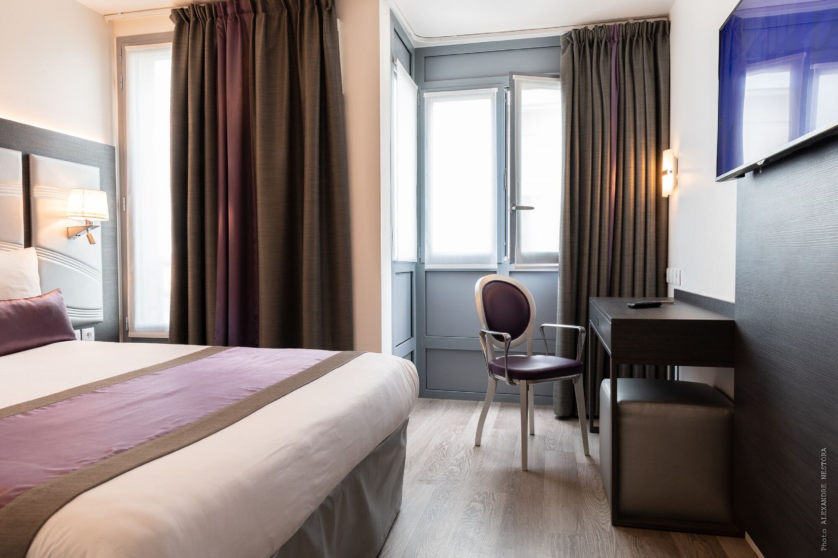 Ett hotellrum med en säng, ett skrivbord, en stol och en tv.
