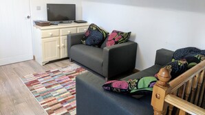 A compact living space with a sofa set, a television on a cabinet, and a wooden staircase. - Apple Loft (Alford)