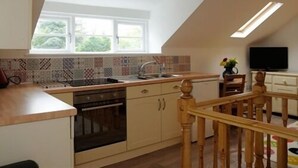 A kitchen with a sloped ceiling, a window, a built-in oven, and a wooden staircase. - Apple Loft (Alford)